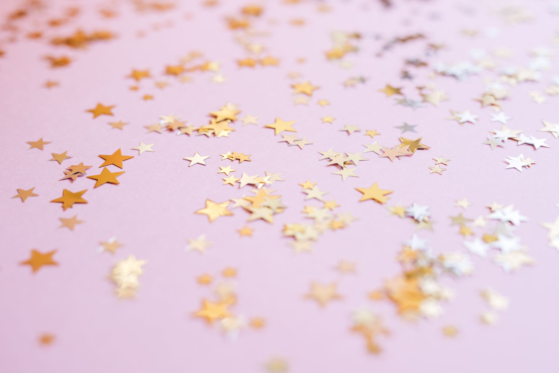 Confettis en forme d'étoiles dorées dispersés sur une surface rose pastel.