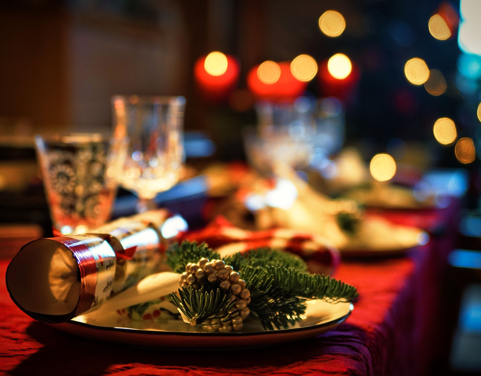 Assiette de Noël décorée d'une branche de sapin et de perles dorées, bougies rouges en arrière-plan