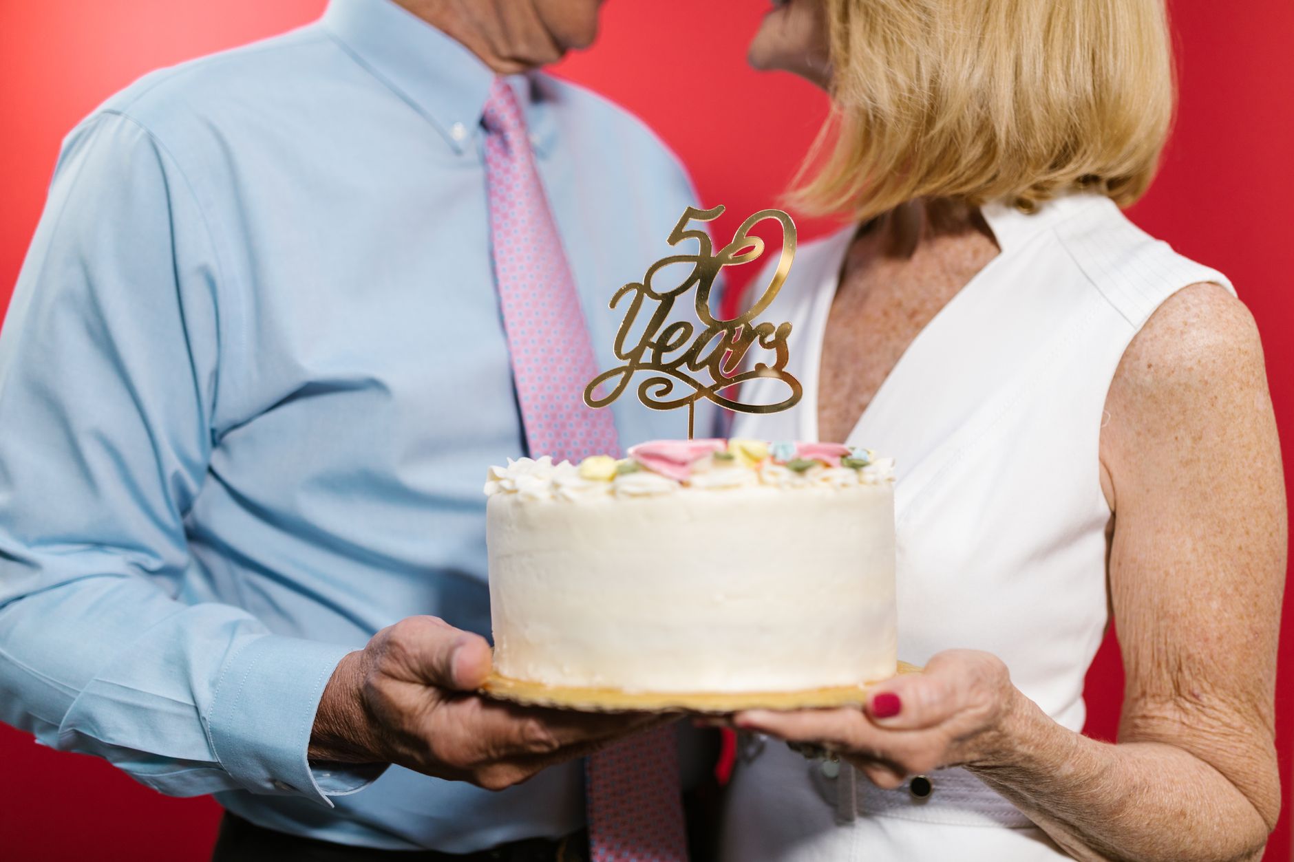 Un couple âgé tient un gâteau d'anniversaire blanc surmonté d'une décoration dorée indiquant 50 ans.
