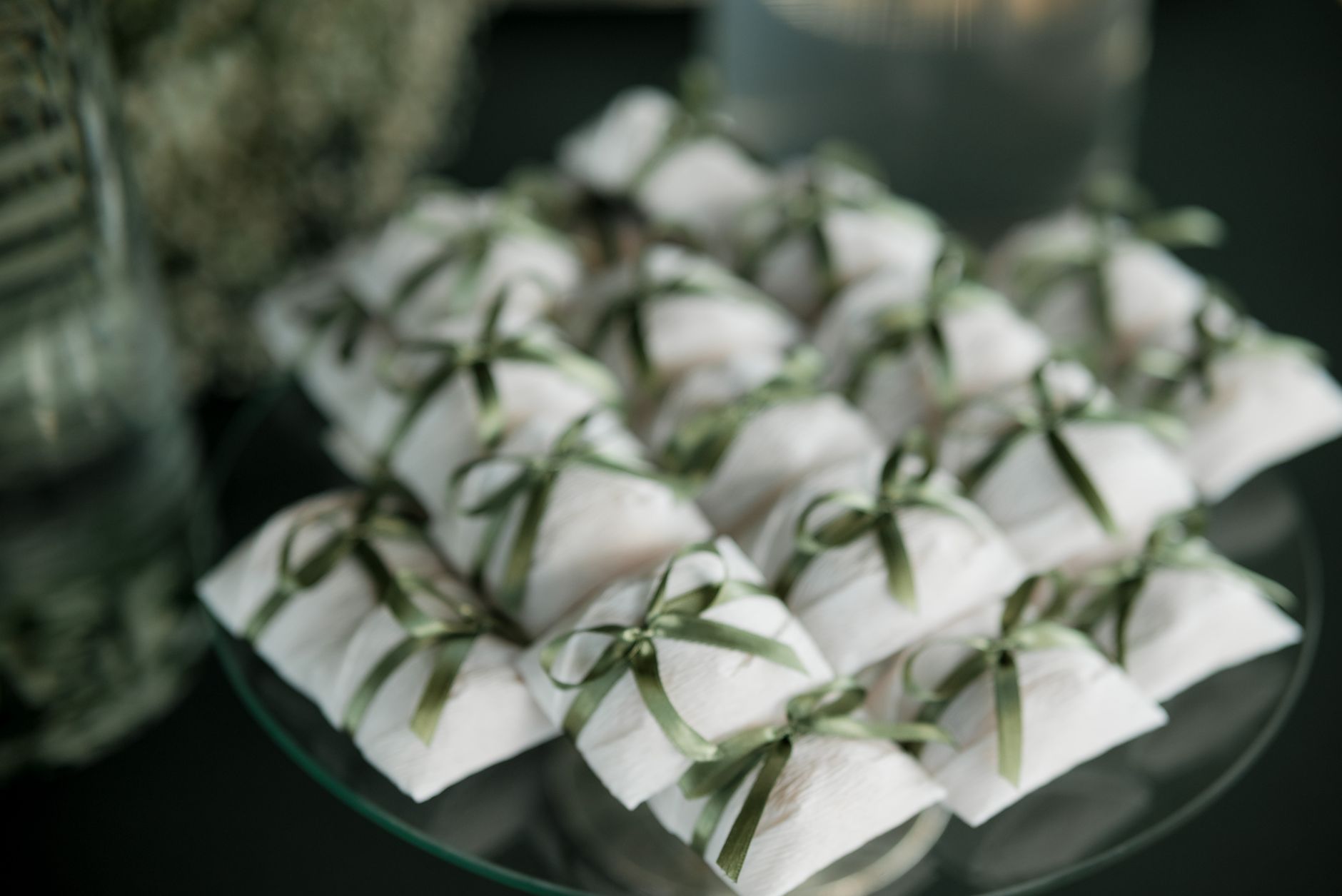 Petits paquets cadeaux blancs noués avec des rubans verts disposés sur un plateau en verre pour un mariage.