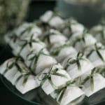 Petites boîtes de cadeaux d'invités emballées dans du papier blanc et nouées avec des rubans verts sur un plateau en verre.